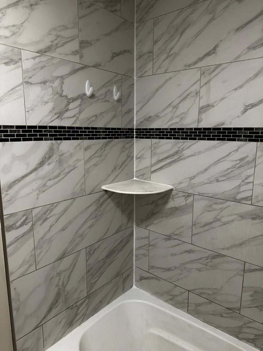 Close-up of marble-look tile tub surround and black accent band