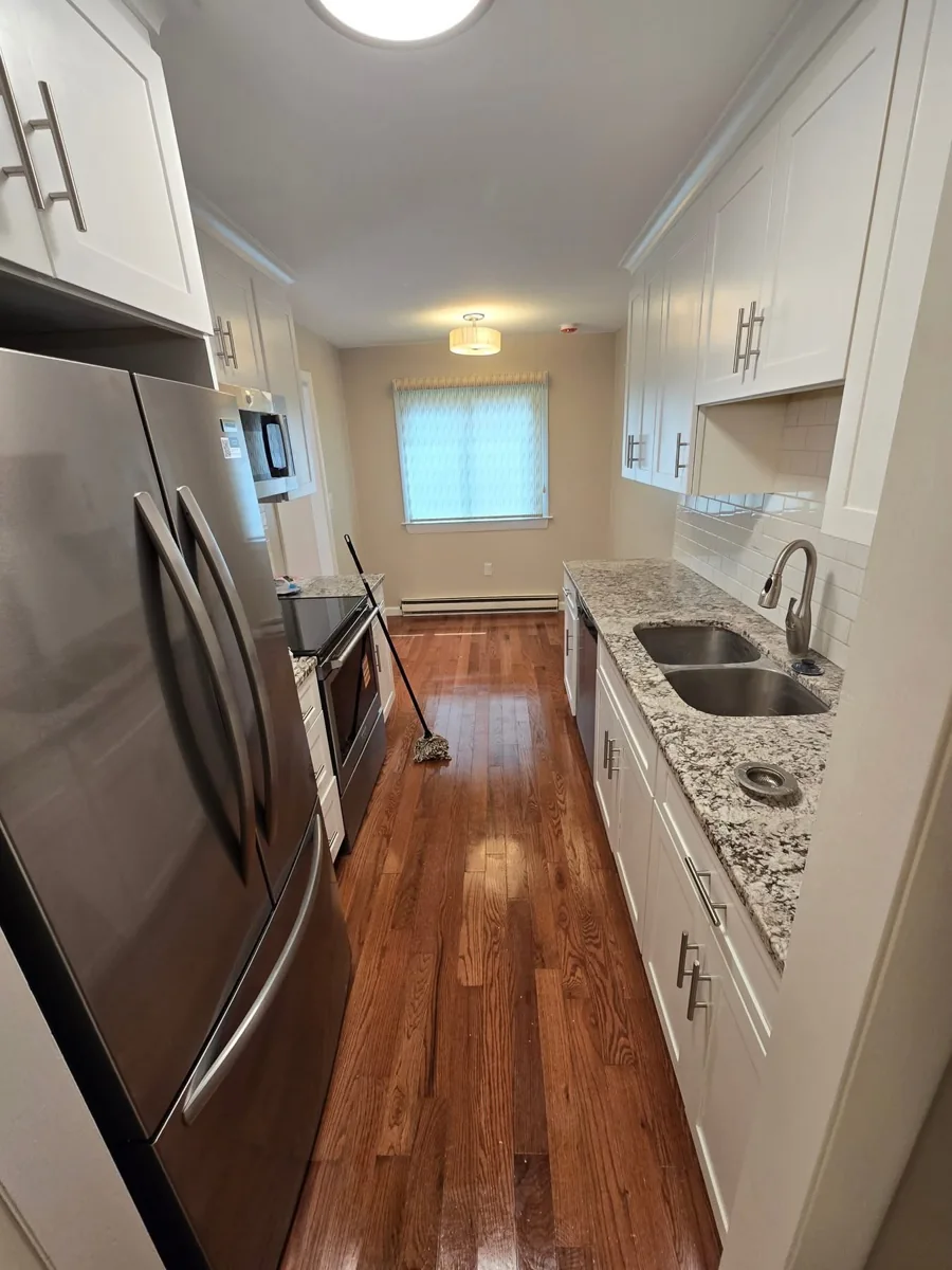 Bright galley kitchen with white cabinetry and wood flooring